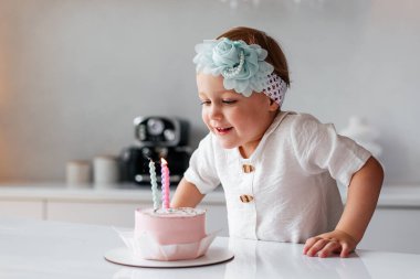 Sevimli üç yaşında bir çocuk doğum gününü kutluyor ve ev yapımı pastaya mum üflüyor.