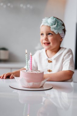 Sevimli üç yaşında bir çocuk doğum gününü kutluyor ve ev yapımı pastaya mum üflüyor.
