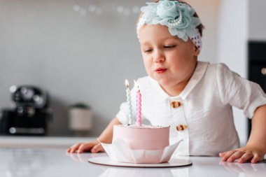 Sevimli üç yaşında bir çocuk doğum gününü kutluyor ve ev yapımı pastaya mum üflüyor.