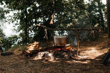 Nehir ve günbatımı adam üzerinde yanan bir ateş üzerinde bir su ısıtıcısı seyahat. Bir kamp ateşi üzerinde pişirme.