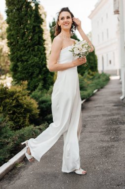 Beyaz elbiseli, uzun boylu, yürüyen gelin elinde bir buket çiçekle..