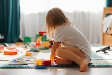 Evde, oyun odasında inşaatçıyla oynayan küçük bir kız. Bebek ve bebek için eğitici bir oyun. Çocuklar oyuncak ev yapar..