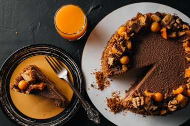 Bıçağın yanındaki masaya konmuş meyve suyu bardağının üst görüntüsü ve beyaz tabakta dilimlenmiş çikolatalı pasta..