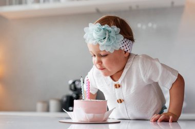 Üç yaşındaki kız doğum günü pastasında mumu üflüyor. Çocuk yıldönümünü ev yapımı çikolatalı pastayla kutluyor..