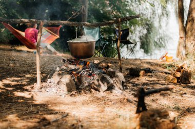 Nehir ve günbatımı adam üzerinde yanan bir ateş üzerinde bir su ısıtıcısı seyahat. Bir kamp ateşi üzerinde pişirme.