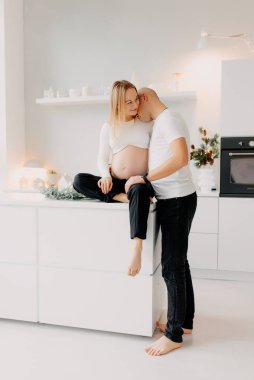 Çift çok mutlu görünüyor. Yakışıklı bir koca, oturma odasının penceresinin yanındaki güzel hamile karısına sarılıyor.