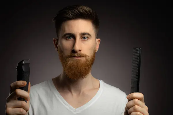 Man shaving whiskers hair by himself, self haircut at home in front of mirror in the bath. Male with long haircut using shaving machine trimmer