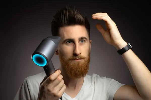 Hair care and grooming concept. Man uses hairdryer, going to make hairstyle after taking shower, drying hair. Copy space.