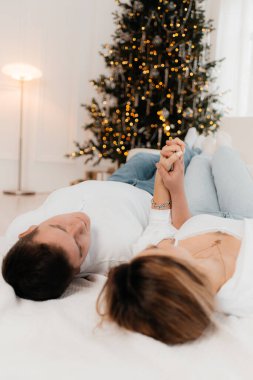 Fotoğraf genç çiftin Noel ağacında kucaklaşmalarını gösteriyor..