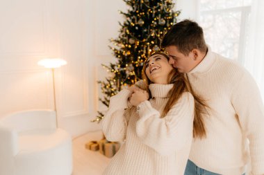 Kafkasyalı erkek ve kadın aşıklar ev içinde tatil ve kış tatilinin keyfini çıkarıyorlar. Birbirlerine aşık çiftler, neşeli dekoratif apartman dairesinde oturuyor ve birlikte mutluluğu hissediyorlar.