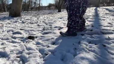 Küçük bir çocuk taze karda yürür. Ceketli bir kız kara basıyor ve ayak izleri bırakıyor. Bacaklar yakın. Yavaş çekim