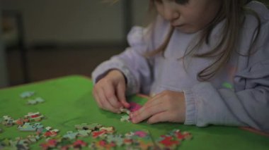 Çocuk bir bulmaca topluyor. Bulmacanın elementleri beyaz bir masanın üzerinde serili. Maç sırasında çocukların elleri. Ev eğlencesi..