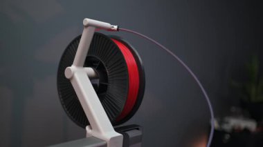 Modern bir 3D yazıcı cihazına monte edilmiş yüksek kalite kırmızı yazıcı ipliği. Yakın plan. Nesne ürün prototipi ve tasarımı için kullanılan tüketici sınıfı termoplastik materyaller.