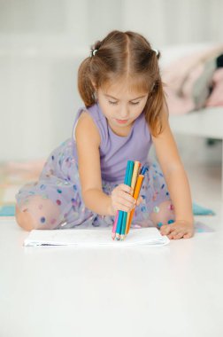 Genç bir kız renkli kalemlerle resim çizmekten zevk alıyor, yaratıcılığını ve neşeli ruhunu gösteriyor.