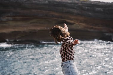 Kaygısız kız uçurum boyunca yürürken kollarını açar. Yüzü yok