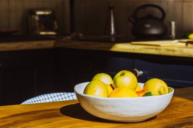 Bir tabak taze mevsimlik meyve, sade bir mutfağın ahşap bir masasında duruyor. Sağlıklı yiyecekler, beslenme, sağlıklı bir yaşam tarzı için vitaminler. Elmalar, portakallar, limonlar, turunçgiller. 