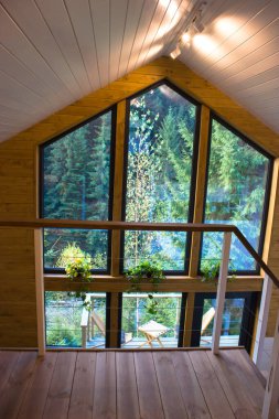 İki katlı ahşap kulübe içeriden kozalaklı çam ağacından yeşil ormanda. Yazlık bir evin panoramik penceresinden inanılmaz bir kalp kırıcı manzara. Modern oturma odası.