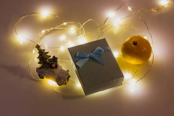 New Year\'s present in a gift box with a bow, LED lights, tangerine in a dark room top view. Greetings for the New Year 2023, Christmas holiday. A magic of winter holidays. Cold season symbols flatly.