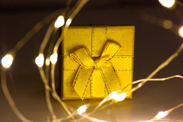 Ledライトガーランドに囲まれた暗い黒の背景に弓で飾られた紙に包まれた黄色のギフトボックス 冬の祭りの背景 2023年クリスマスのコンセプト — ストック写真