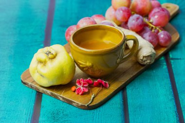 Uçan dairenin üzerinde sarı bardakla güzel bir sonbahar hayatı. Bir demet kırmızı üzüm, olgun agave, kesme tahtasında zencefil kökü. Düşmüş meşe, akçaağaç yaprakları. Tahta yeşil zümrüt arkaplan metin için boşluk.
