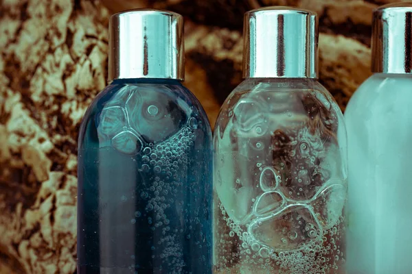 Plastic cosmetic bottles with natural cosmetic in travel containers - shower gel, shampoo with bubbles inside, body lotion in miniature containers against a rock background close up. Face body care.