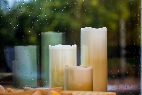 一套白色的黄色石蜡人造高蜡烛贴在潮湿的窗户上 上面有水滴 雨下在窗外装饰舒适舒适的家 秋天寒冷的雨天仍有生命 秋季季节 — 图库照片