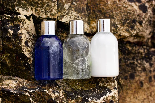 Travel kit. Cosmetic products set in travel containers against rocky cliff backdrop. Natural face body skin care products. Shampoo shower gel lotion against stone background. Stylish cosmetic bottles.