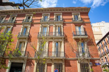 Madrid, Spain. 7 May 2022. A corner of a red brick building in sunlight. Facade of well-preserved old house in classical style. Windows and balconies with wooden shutters. Vintage architecture in city