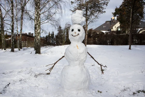 Ugly smiling snowman made by children from the first snow. Winter entertainment for children in the fresh air on a frosty day. Symbol of winter, frost, new year and Christmas. Melting snow snowmen
