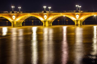 Bordeaux, Paris. 5 Ekim 2022 Pont de Pierre taş köprüsü gece iki nehir kıyısını birbirine bağlıyor. Suyun pürüzsüz yüzeyinde sokak lambalarının yansıması. Uzun pozlama. Seyahat hedefi.