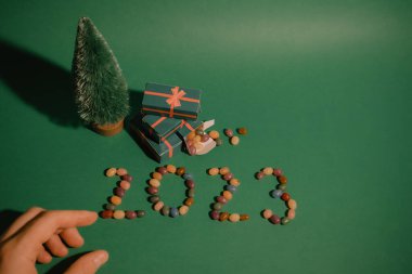 Yeşil Noel arkaplanı, dekoratif çam ağacı, hediye kutuları ve kadın eli. Mutlu Noeller ve renkli şekerlerden yapılmış 2023 sözcüğüyle yeni yıl tebrik kartı. Kış tatili duvar kağıdı.