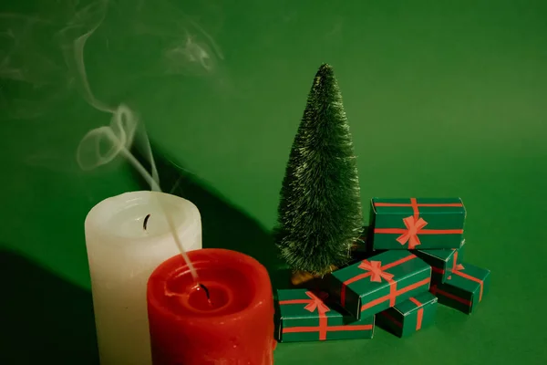 Vintage green Christmas card with a decorative toy pine tree and gift boxes, presents for winter holidays. Red and white extinguished candles, make a wish concept. New Year\'s Eve 2023 2024 celebrate.