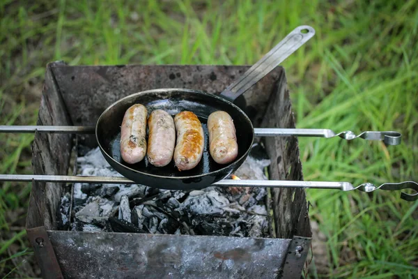 生ソーセージを焼く ソーセージ ワイナー 肉を上からのピクニックの火の眺めで黒いグリドルで揚げたものを食欲をそそる 公園の森の中で屋外で料理 石炭の上のバーベキュー 開いて火の上のストリートグリルを平らに — ストック写真