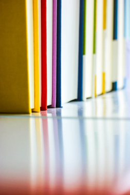 Bir kitap rafında üst üste yığılmış kırmızı, sarı, mavi ve menekşe renkli kitaplardan oluşan bir yığın. Edebiyat, bilgi, eğitim, bilim konsepti. 2022 'ye dönüyoruz. Yazdırma kitapları yansımaları.
