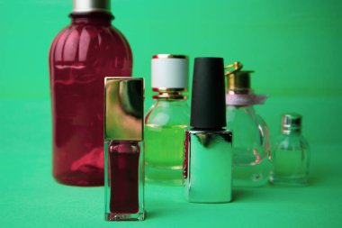 Cam şişe eau de tuvalet parfümleri, mavi yeşil arka planda kokular. Kırmızı şişede krema losyonu, kavanoz. Merhem, tüp içinde parlak kırmızı ruj, oje. Çeşitli profesyonel kozmetik ürünleri