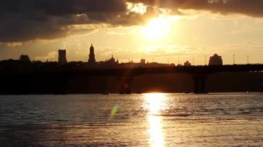 Akşam şehrinin silueti karanlığa gömülüyor. Ukrayna 'nın başkenti Kyiv panoramik bir köprü manzarası, Dnipro nehrinin suyu, sarı günbatımına karşı binalar. Bir metropolde ışıklar sönüyor, elektrik kesiliyor.