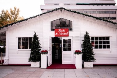 Madrid, İspanya. 30 Kasım 2022 Noel Baba 'nın beyaz ahşap evi. Yeni yıl için ev dekorasyonu ürünleri ve sokakta Noel ağaçları. Tienda de Navidad yazılı kırmızı masa