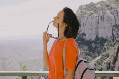 Kısa bakımlı güzel esmer kız profil olarak güneş gözlüğünü çıkardı. Dişi turist dağlarda tek başına seyahat eder. Yolculuğun ve temiz havanın tadını çıkarıyorum. Sokakta gezen insanlar.