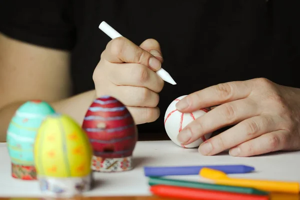 Coloring Easter eggs with wax crayons at home. White Easter egg in women's hands before dyeing colors. Easter egg master class. Artistic work, handmade DIY. People preparing for Easter in April 2023.
