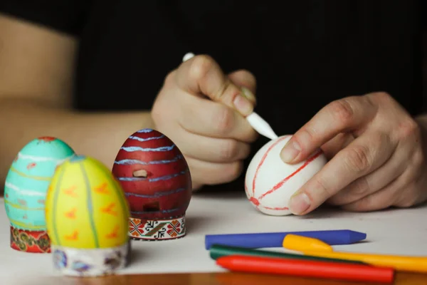 Coloring Easter eggs with wax crayons at home. White Easter egg in women's hands before dyeing colors. Easter egg master class. Artistic work, handmade DIY. People preparing for Easter in April 2023.
