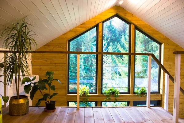 Second floor of two-story wooden cottage inside in coniferous spruce pine green forest. Amazing heartbreaking view from the panoramic large window of a summer country house. Modern living room indoors