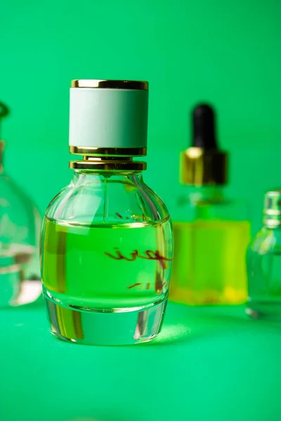 A glass bottle of eau de toilette perfume, perfumes fragrances on green vertical background. Cosmetic essential in bottles. Female beauty concept. Set of vials for perfume. Smells for women.