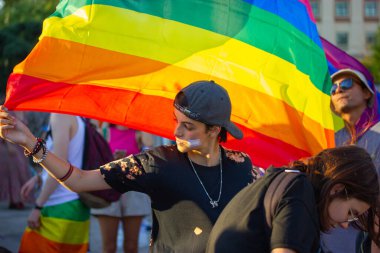 Madrid, İspanya. 26 Temmuz 2022 'de Lezbiyen bir kız, yazın düzenlenen eşcinsel geçit töreninde LGBT topluluğunun sembolü olarak gelişmekte olan bir gökkuşağı bayrağı taşıyor. Şehir caddesinde gurur ayı partisi kutlaması. Bayrağı olan insanlar.