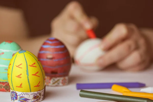 A person is painting Easter eggs with colored crayons. Preparing for Easter religious festivities 2023. Hobby, leisure, spring break at home. Family holiday. Preparing decorations. Festive food.