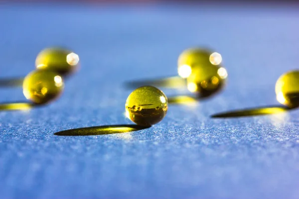 stock image Yellow colored fish oil pills, tablets, omega 3 gelatin capsules lie on blue table leaving contrasting long shadows flatly. Medical, health care, medicine treatment minimalistic background top view.