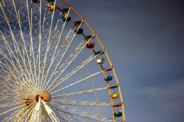 Mavi arka planda şeffaf kabinleri olan beyaz bir dönme dolap. Şehir eğlencesi. Luna park oyunları, çocuklar için eğlence, atlı karınca. Aşağıdan yüksek inşaat manzarası. Kumarbazlar için bir cazibe.. 