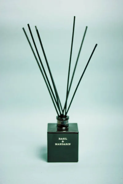 Aroma diffuser with aroma of basil and mandarin in a black glass jar with bamboo sticks on a blue vertical background. A fragrance for home flatly. Decor, details for a cozy modern interior.