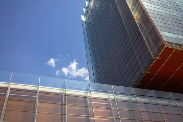 Modern tall building with glass facade against blue sky in sunny day. Office building of a company in an urban space, city center. Architecture of a Spain. Details of buildings perspective skyscraper.