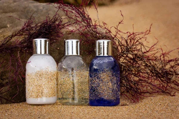 Plastic bottles, containers with eco cosmetics - shampoo, shower gel, body lotion for facial skin care - on the sandy coast among the red seaweed. Natural cosmetics for a vacation by the sea in summer