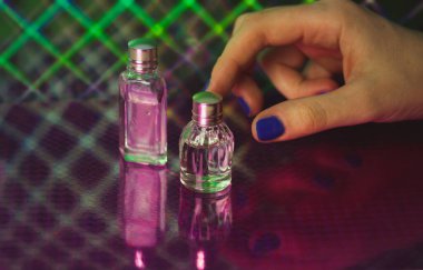 Bir kadının mavi manikürlü eli cam bir şişe parfüm suyuna uzanır. Kadınlar için parfüm seçimi. Kozmetik ürünleri alıyorum. Minyatür kaplarda farklı parfümler. Kadın güzellik aletleri.